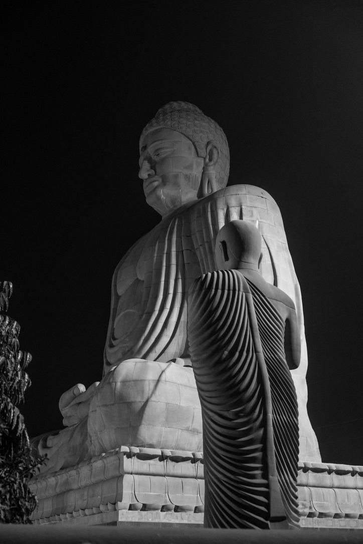 Grande statua del Buddha illuminata di notte, con un monaco in preghiera davanti